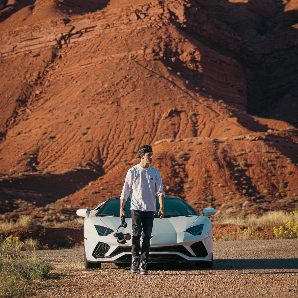 Behind the scenes — filmmaker with gimbal and white Aventador in red rock desert